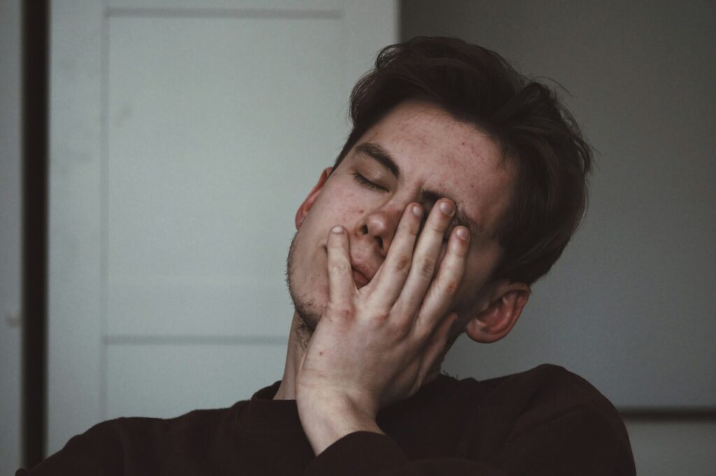 Person holding their hand to their face with eyes closed, experiencing headache pain